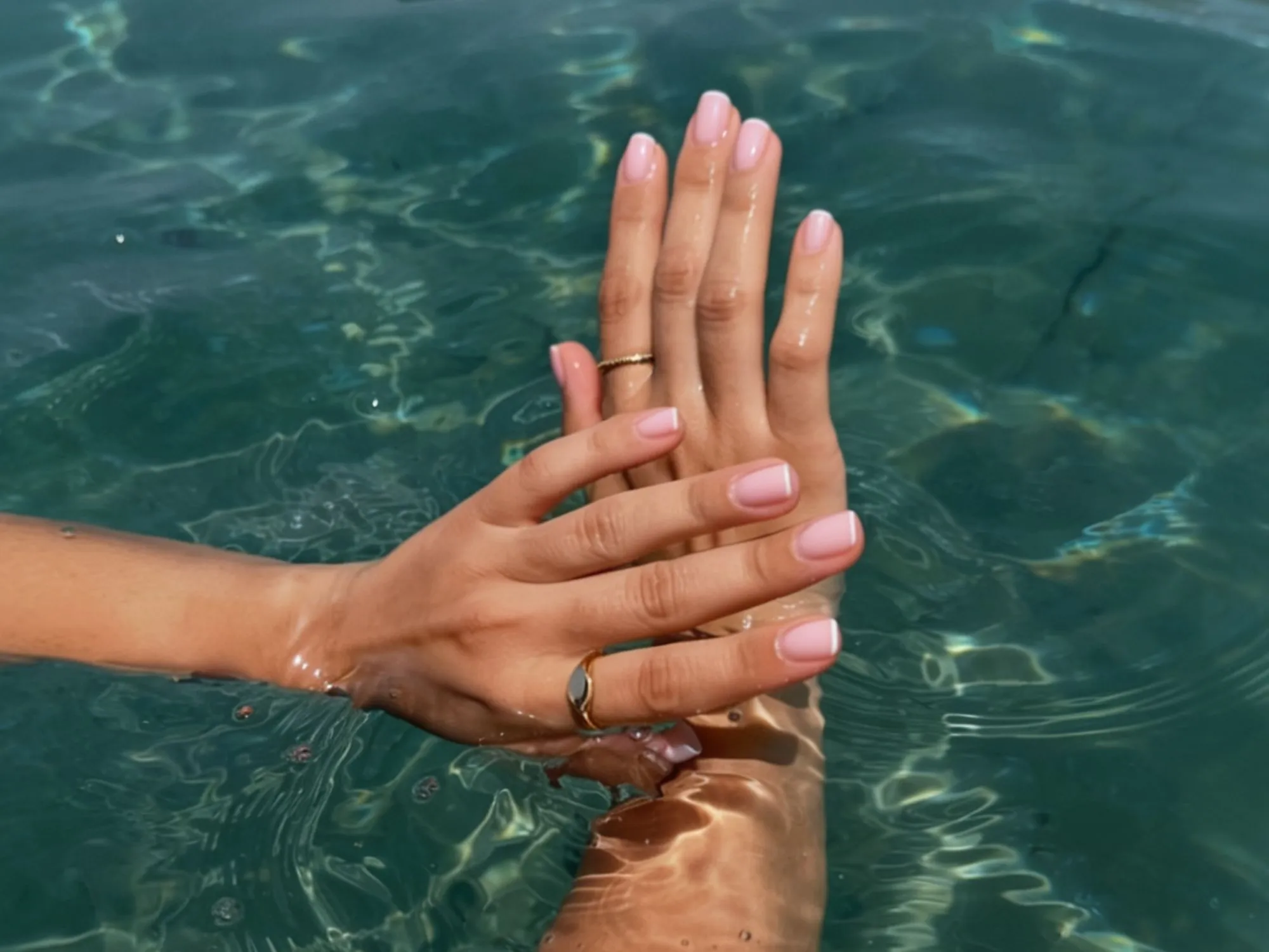Fotografija prikazuje nježne ženske ruke s elegantnom, prirodnom manikurom u nježno ružičastoj nijansi. Slika prikazuje kvalitentnu njegu noktiju ljeti.
