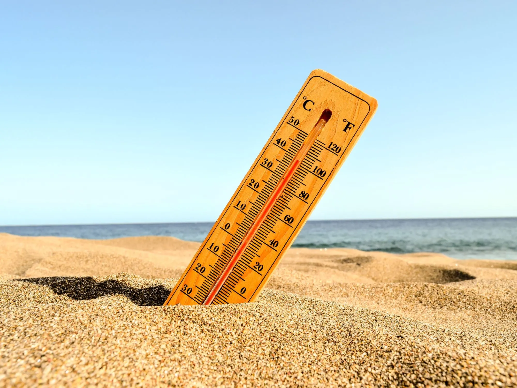 Termometar zaboden u vrući pijesak na plaži prikazuje visoke temperature tijekom toplinskog vala.