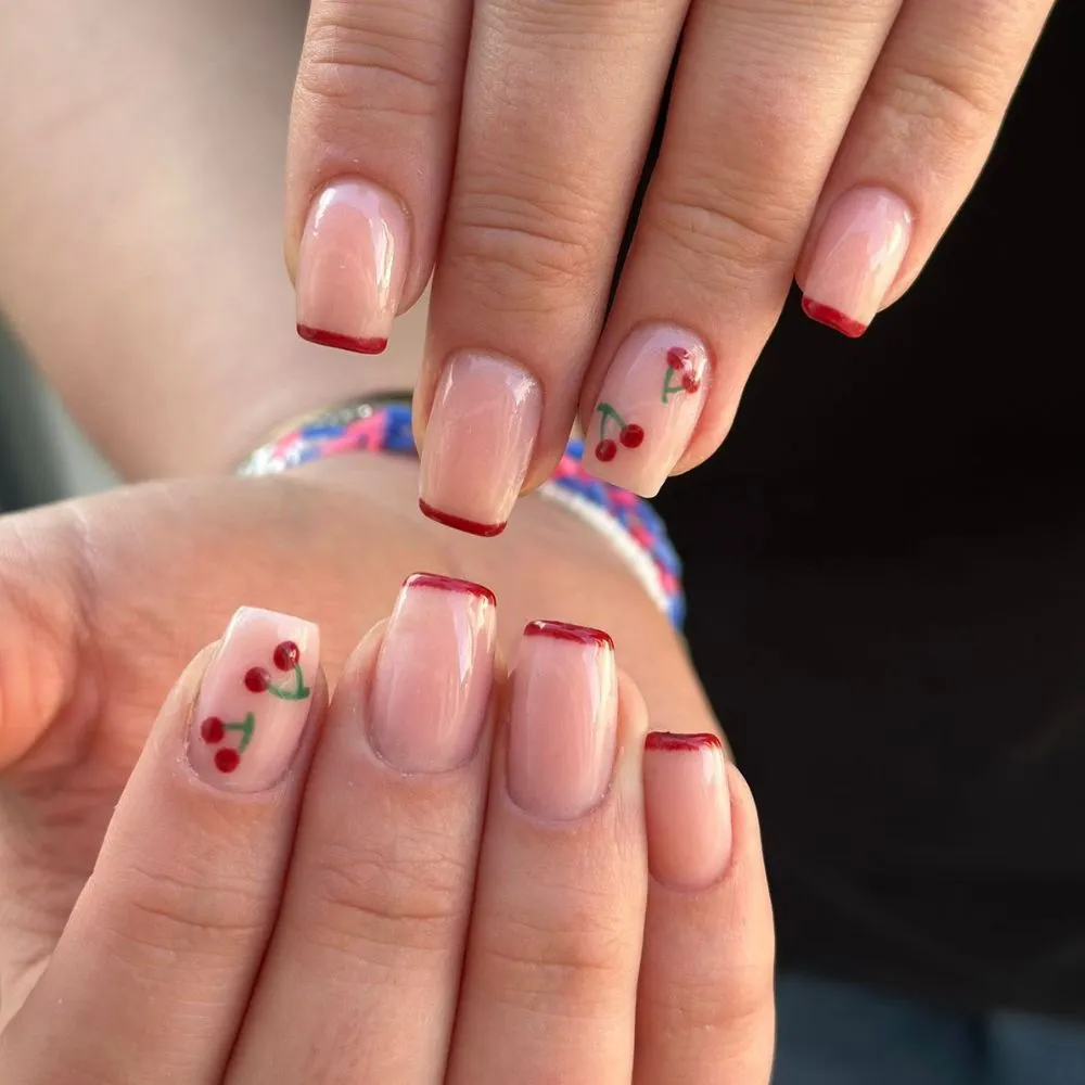 Moderni ljetni nail art s motivom crvenih trešnjica na nude bazi noktiju sa tankim crvenim frenchom.